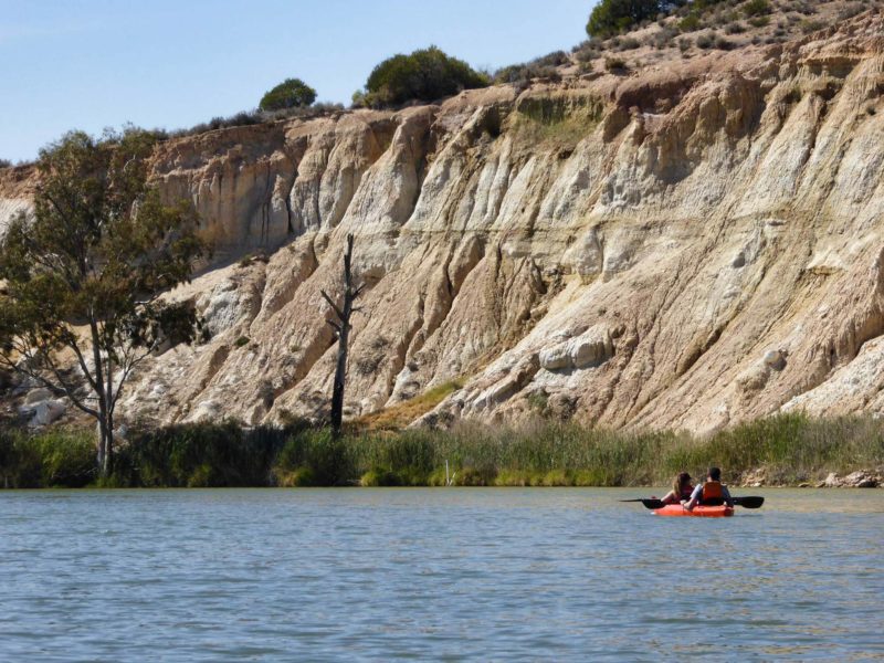 kayakers on river by tall cliffs