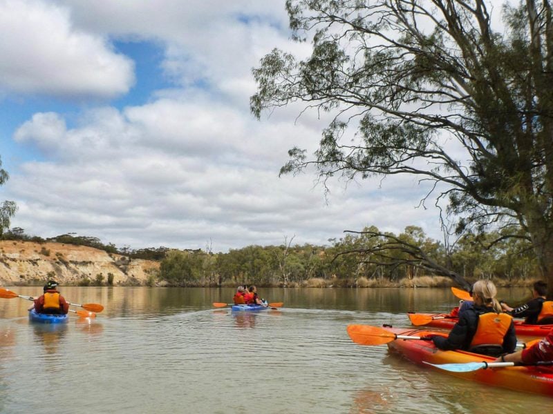 paddlers move from creek to river, by cliffs