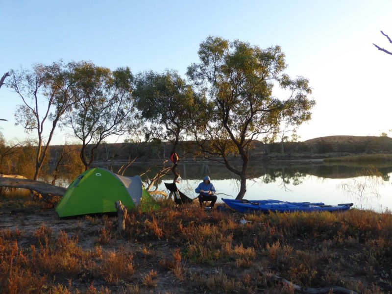 camper at dawn, sitting between tent and kayaks