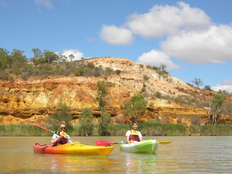 kayakers on river by cliffs