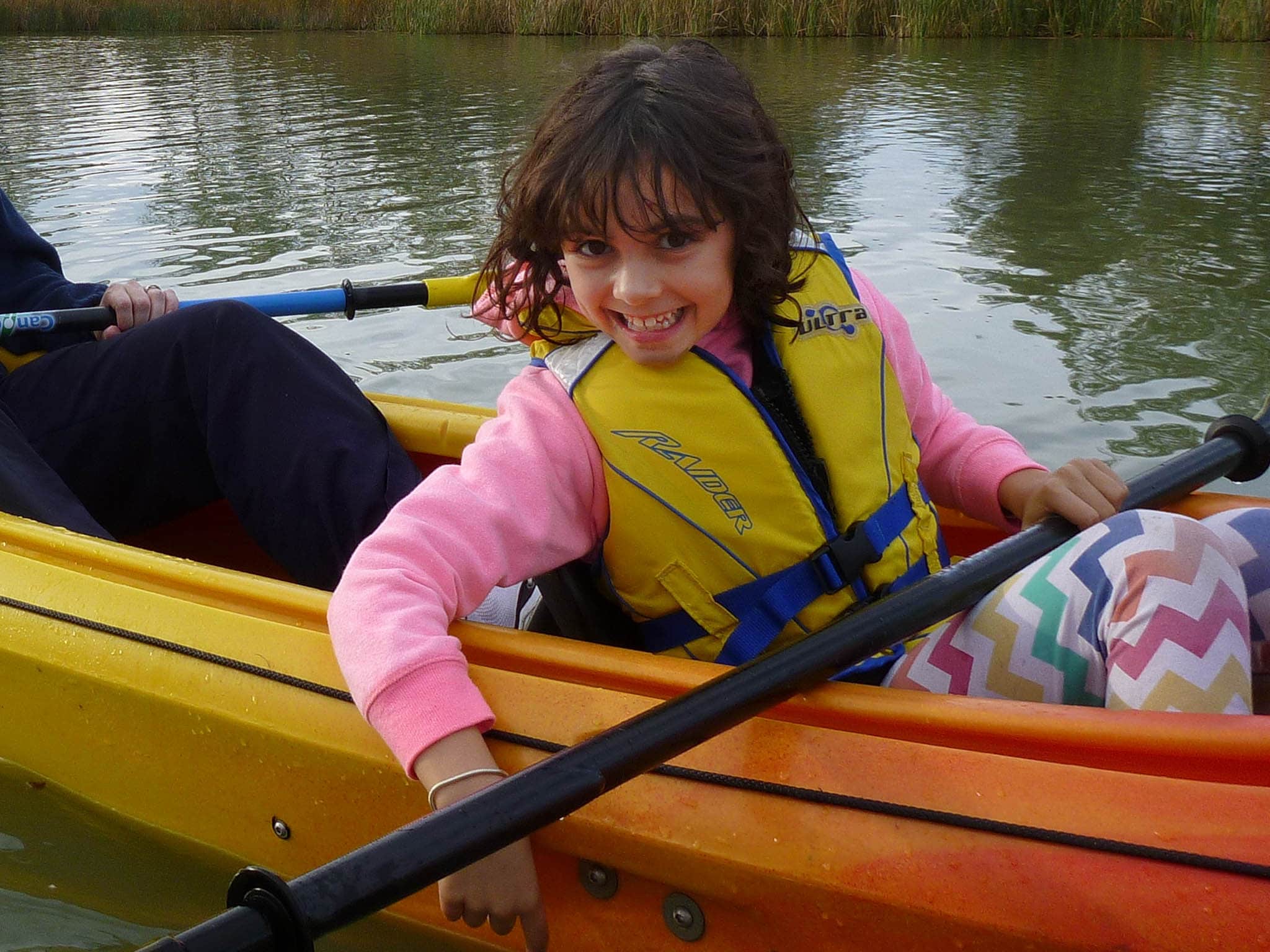 cute girl in life jacket, with paddle sits in front of double kayak