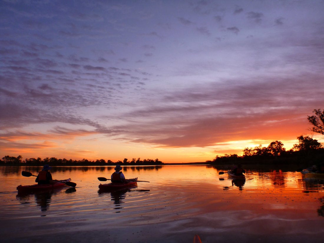 3 kayakers float, watching a magnificent sunset