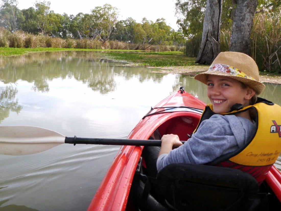 smiling girl in front of double kayak, looks back over shoulder, in narrow creek