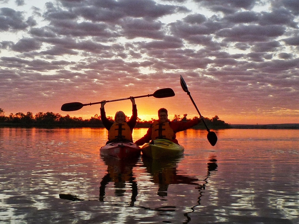 silhouette of kayakers in front of a sunrise