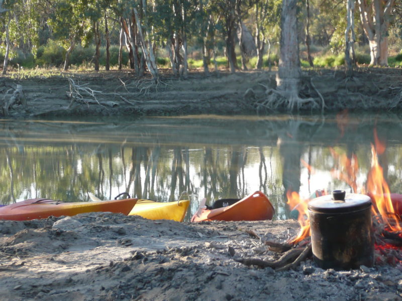 campfire and billy, with kayaks on riverbank in background