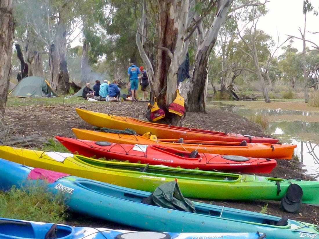 outdoor education group around campfire, with kayaks in foreground