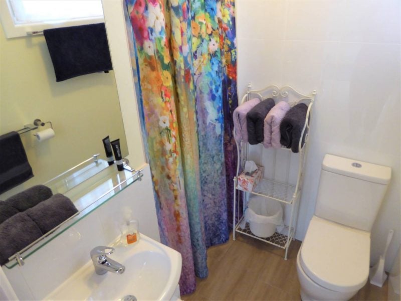 Modern Ensuite bathroom with toilet, basin and shower, and towels stacked on baker's stand