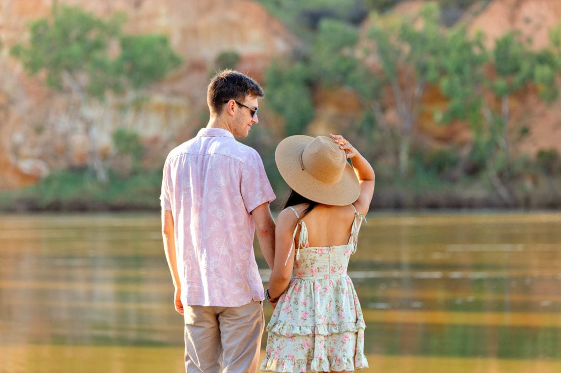 Young couple stand on river's edge looking at cliffs