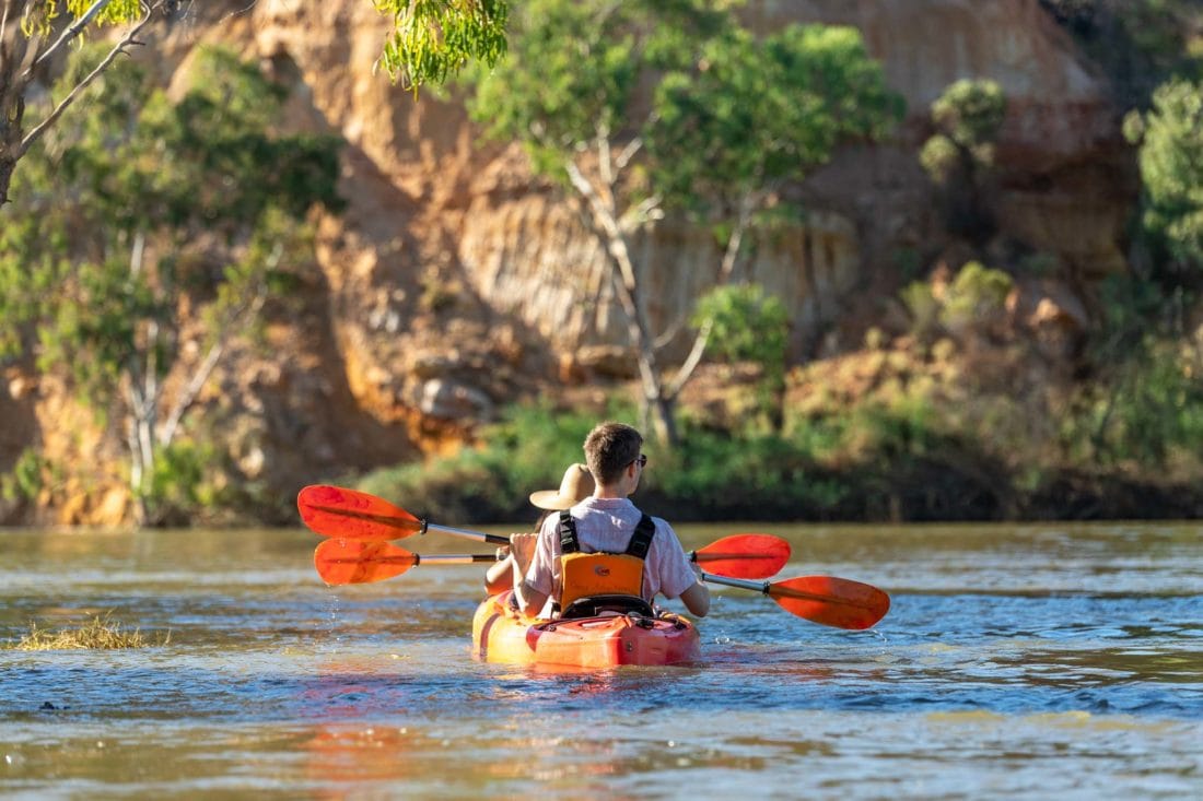 Couple in a double kayak, in front of colourful cliffs