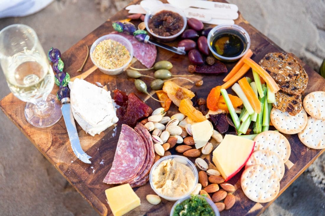 Gourmet Platter on picnic table, including pesto, nuts, hommus, cheeses, quince paste, dried fruit, crackers, olives, caper berries, dukkah, olive oil and chutney