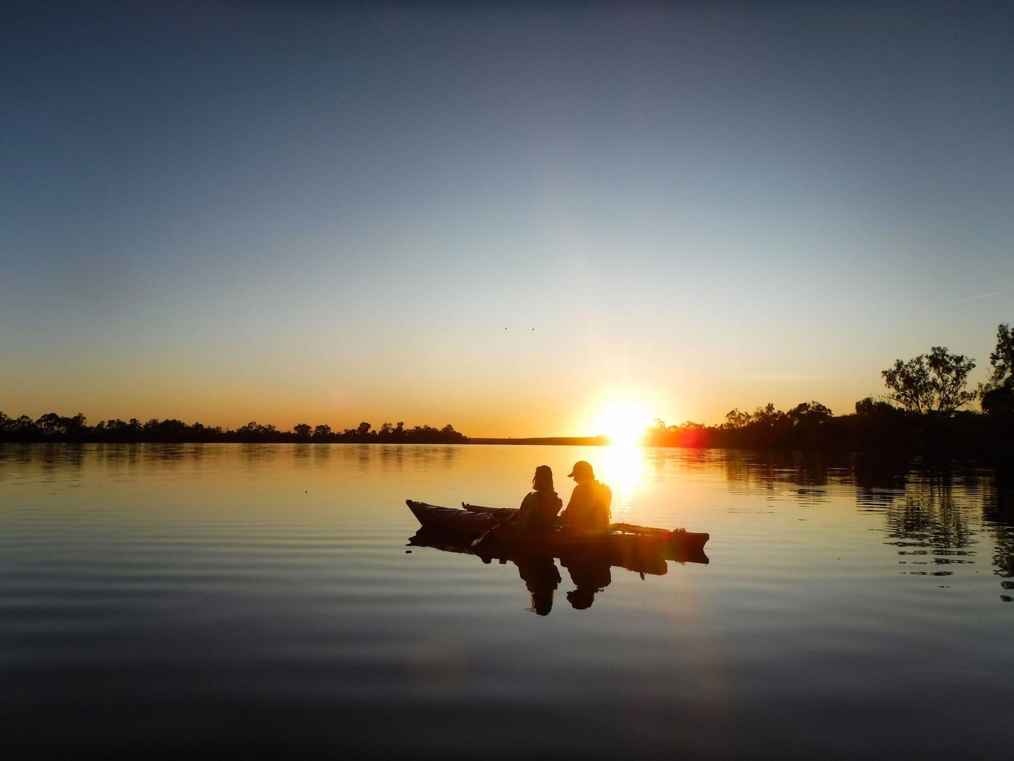 Couple in double kayak silhouetted against beautiful sunrise.